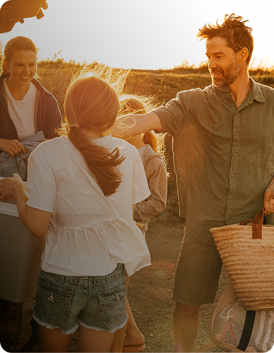 Family unloading beach gear from a car at sunset.