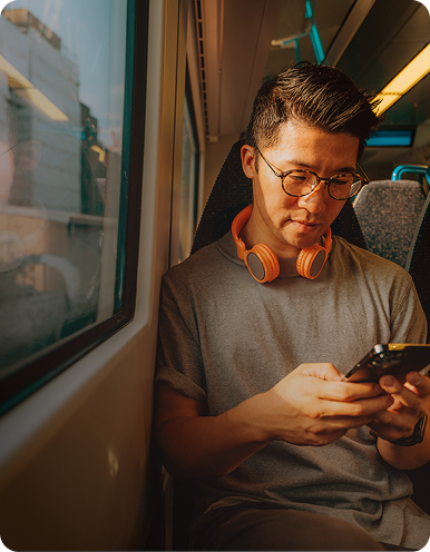 Person sitting on a train looking at a smartphone, with headphones on.