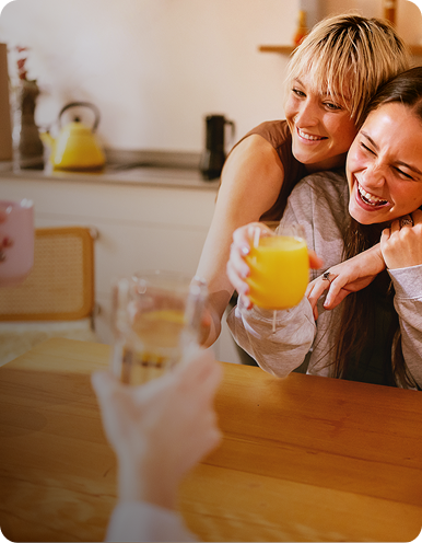 Friends gathered around a kitchen table, laughing and raising drinks in a toast.