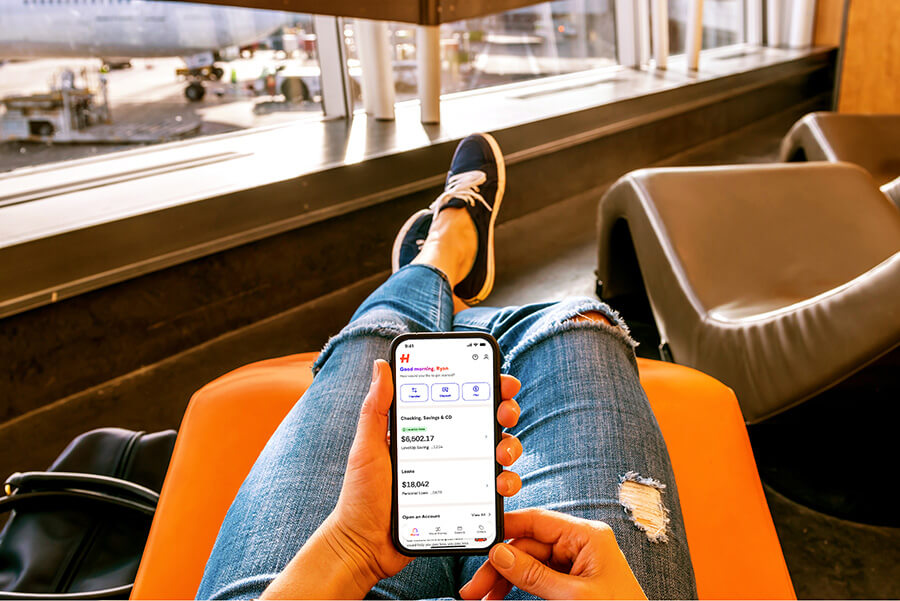 Person reclining in an airport lounge chair while holding a smartphone open to the Happen Bank app.
